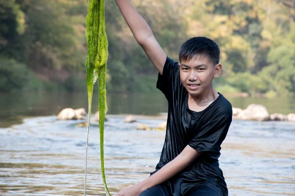 Asian schoolboy holding freshwater algae from diving into the river and pulling it up to study the fertility of the river's nature and including to do freshwater algae in his environment project work.