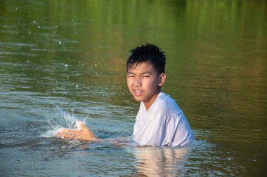 Asian boy is spending his freetimes by diving, swimming, throwing rocks and catching fish in the river happily, hobby and happiness of children concept, in motion.