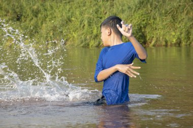 Asian boy is spending his freetimes by diving, swimming, throwing rocks and catching fish in the river happily, hobby and happiness of children concept, in motion.