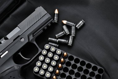 Automatic black 9mm pistol and bullets on black leather background, selective and soft focus, copy space.