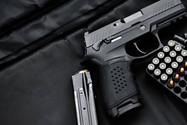 Automatic black 9mm pistol and bullets on black leather background, selective and soft focus, copy space.
