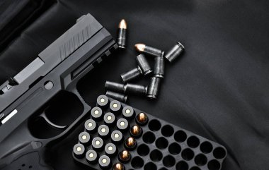 Automatic black 9mm pistol and bullets on black leather background, selective and soft focus, copy space.