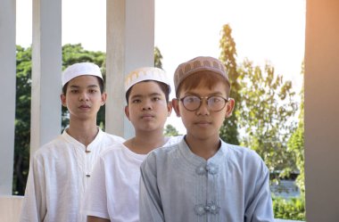 Group of Asian muslim or islamic boys in priest suit and wear hat, standing together in front porch of the mosque during their religious activity, concept for teenagers lifestyle around the world.