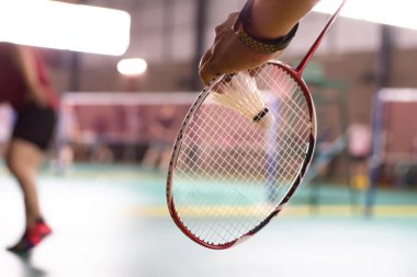 Badminton oyuncusu, raketi ve beyaz kremalı mekikçiyi sahanın diğer tarafına götürmeden önce kalenin önünde tutuyor..