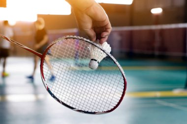 Badminton oyuncusu, raketi ve beyaz kremalı mekikçiyi sahanın diğer tarafına götürmeden önce kalenin önünde tutuyor..