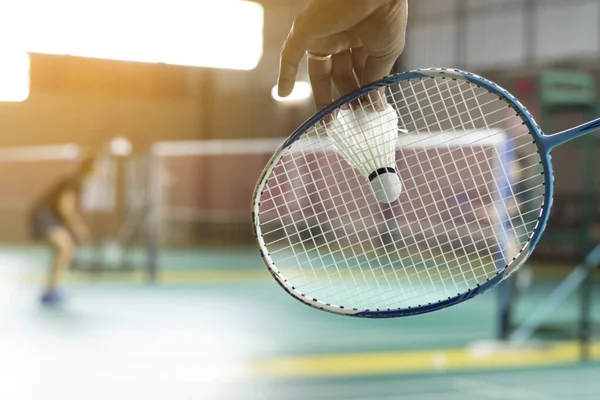 stock image Badminton player holds racket and white cream shuttlecock in front of the net before serving it to another side of the court.