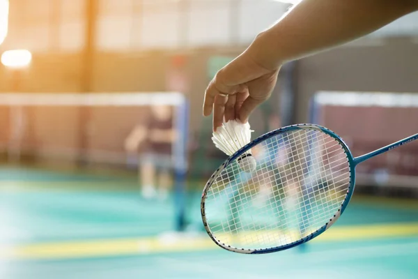Badminton oyuncusu, raketi ve beyaz kremalı mekikçiyi sahanın diğer tarafına götürmeden önce kalenin önünde tutuyor..