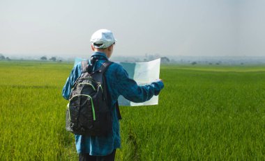 Çocuk, elinde harita ve dürbünle hafta sonu boyunca çeltik tarlasının tepesinde dikilip bilgi okuyor ve detaylarını okuyor. Doğa ve tarım arazisi araştırması kavramı..