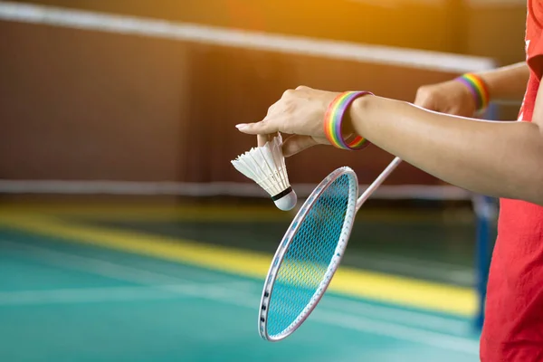 Badminton player wears rainbow wristbands and holding racket and white shuttlecock in front of the net before serving it to player in another side of the court, concept for LGBT people activities.