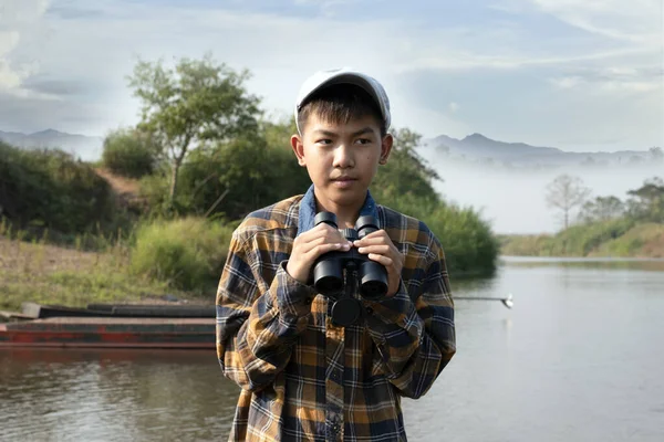 Ekose Gömlekli Kepli Asyalı Bir Çocuk Elinde Dürbünle Nehir Kenarına — Stok fotoğraf