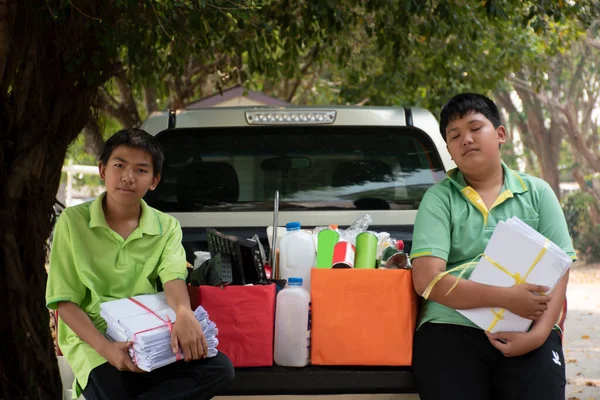 Asian boy in green t-shirt is separating different types of trash into color-coded boxes in the back of a pickup truck before leading them to sell and generate income after their school holidays.