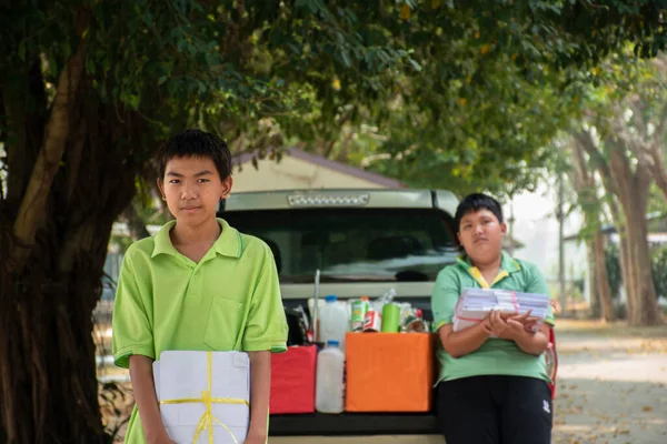 Asian boy in green t-shirt is separating different types of trash into color-coded boxes in the back of a pickup truck before leading them to sell and generate income after their school holidays.