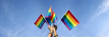 Gökkuşağı bayrakları bulutlu ve mavi arka planda el ele tutuşuyor, tüm insanları LGBT insanlarını desteklemeye ve dünyadaki cinsiyet çeşitliliğine saygı göstermeye çağıran kavram..