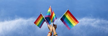 Gökkuşağı bayrakları bulutlu ve mavi arka planda el ele tutuşuyor, tüm insanları LGBT insanlarını desteklemeye ve dünyadaki cinsiyet çeşitliliğine saygı göstermeye çağıran kavram..