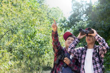 Kırmızı şapkalı ve ekose gömlekli genç Asyalı oğlanlar ellerinde dürbünle kuşları, orman hayvanlarını ve arkasında yaşayan diğer böcekleri izliyorlardı..