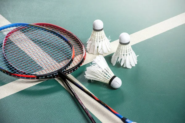 Badminton rackets and white cream badminton shuttlecocks after playing or after games on green floor in indoor badminton court, soft focus, concept for badminton lovers around the world.