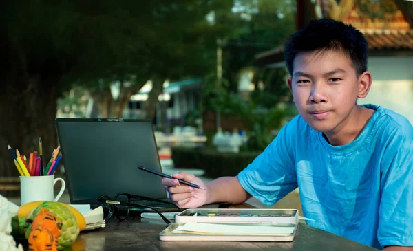 身穿蓝色T恤的亚洲男孩坐在那里 利用水彩画来打发业余时间 这是全世界青少年暑假的概念 — 图库照片