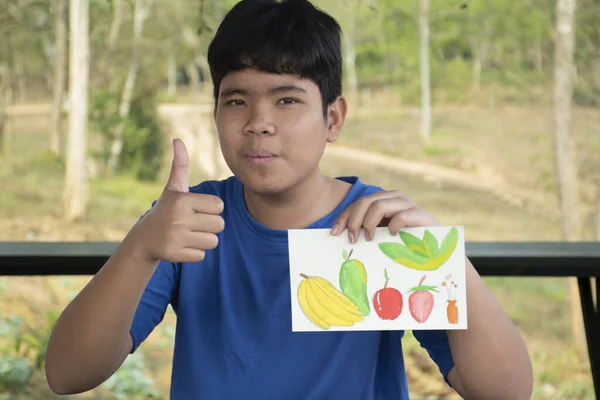 一个身穿休闲深蓝色衣服的男孩正在展示他的绘画和绘画 他在暑假的阳台上的桌子上 用一个油漆盒里的小水彩画长条展示他的绘画和绘画 — 图库照片