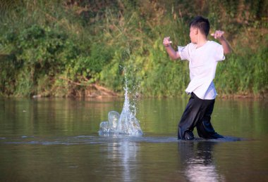 Beyaz tişörtlü Asyalı çocuk boş zamanlarını dalarak, yüzerek, taş atarak ve nehirde mutlu bir şekilde balık tutarak geçiriyor..