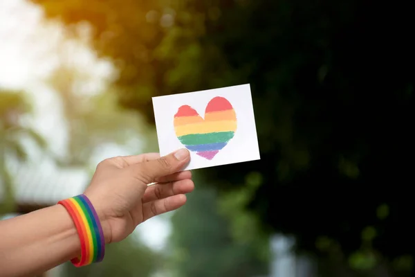 Rainbow heart card holding in hand which has rainbow wristband  around it, concept for LGBT people celebrations in pride month, soft and selective focus.