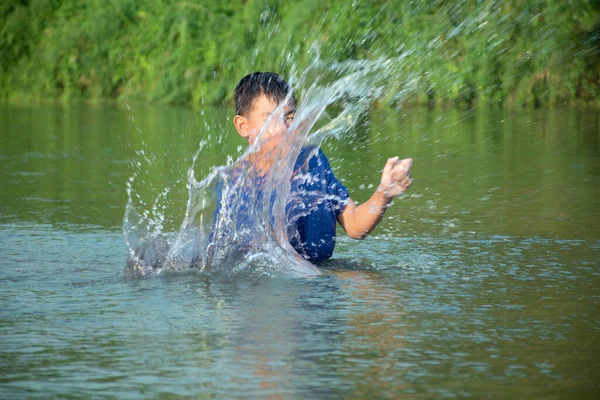 身穿蓝色T恤的亚洲男孩正在享受他的闲暇时光 他们在河里潜水 扔石头 快乐地钓鱼 他们的兴趣爱好和孩子们的快乐观念也在不断变化 — 图库照片