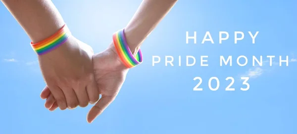 stock image 'Happy Pride Month 2023' and gay couple hands on bluesky background, concept for LGBT people celebrations in pride month, june, around the world.