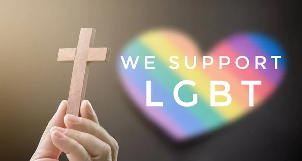 在模糊的彩虹背景下 木制十字与 我们支持男女同性恋 双性恋和变性者 手牵着手 这是全世界支持男女同性恋 双性恋和变性者自豪月庆祝活动的理念 — 图库照片