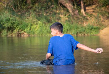 Mavi tişörtlü Asyalı çocuk boş zamanlarını dalarak, yüzerek, taş atarak ve nehirde mutlu bir şekilde balık tutarak geçiriyor..