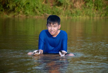 Mavi tişörtlü Asyalı çocuk boş zamanlarını dalarak, yüzerek, taş atarak ve nehirde mutlu bir şekilde balık tutarak geçiriyor..