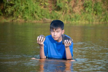 Mavi tişörtlü Asyalı çocuk boş zamanlarını dalarak, yüzerek, taş atarak ve nehirde mutlu bir şekilde balık tutarak geçiriyor..