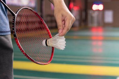 Badminton oyuncusu, raketi ve beyaz kremalı mekikçiyi sahanın diğer tarafına götürmeden önce kalenin önünde tutuyor..