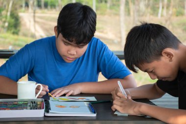 Asyalı çocuklar boş zamanlarını vakalarda suluboya barlar, yazın gençlerin aktiviteleri ve suluboya resim dersleri konsepti kullanarak çizim, resim ve boyama yaparak geçiriyorlar..