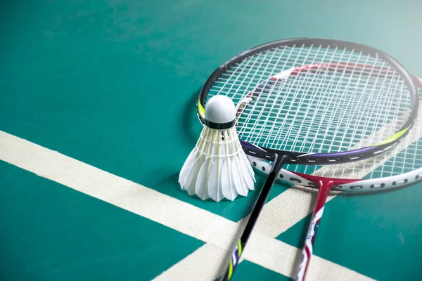 Badminton oyuncusu, raketi ve beyaz kremalı mekikçiyi sahanın diğer tarafına götürmeden önce kalenin önünde tutuyor..