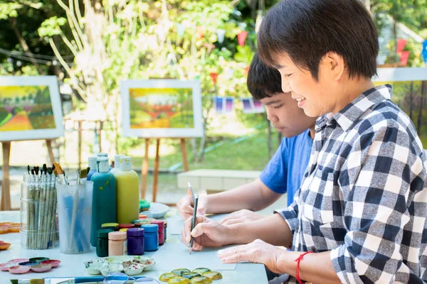 stock image Asian boys are spending their free times with drawing, sketching, coloring and painting by using watercolor bars in cases, teenagers activity in summer and watercolor lesson concept.