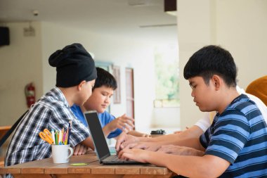 Bir grup Asyalı çocuk birlikte oturup okul ödevlerini yapıyorlar. Web sitesinde önemli bilgileri araştırıyorlar. Laptop kullanıyorlar ve birbirlerine danışıyorlar.