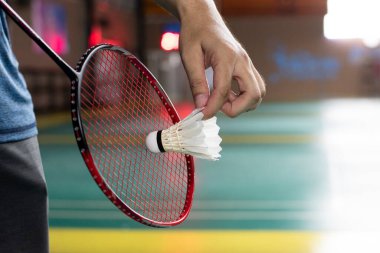Badminton oyuncusu, raketi ve beyaz kremalı mekikçiyi sahanın diğer tarafına götürmeden önce kalenin önünde tutuyor..