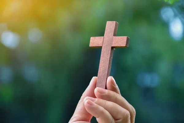 Wooden cross holding in hand with green and fresh forest background, concept for love of god in people around the world.