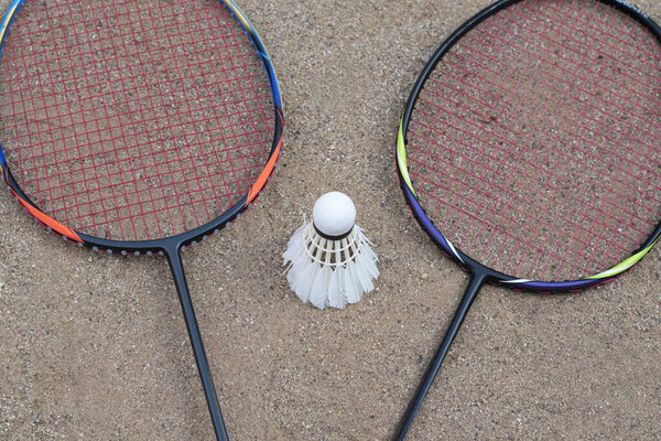 Badminton equipments, rackets and white cream shuttlecocks, on sand floor of outdoor badminton court, selective focus, concept for outdoor activity and outdoor sports for health.