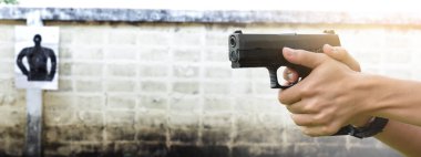 9mm 'lik tabanca nişancının elinde. Atış poligonunun ilerisindeki hedef kâğıdını hedef alıyor. Yumuşak ve seçici bir odak noktası..