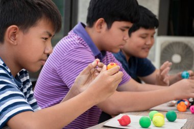 Asyalı çocuklar birlikte oturur ve plastik kalıpları kullanarak öğrenirler. Soldaki çocuğa odaklanırlar. Dünyanın dört bir yanındaki çocukların boş zaman ve hobi aktivitelerine odaklanırlar..