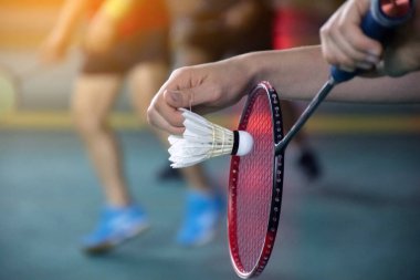 Badminton oyuncusu, badminton sahasının diğer tarafına atmadan önce beyaz badminton topu ve badminton raketini ağın önünde tutuyor. Yumuşak ve seçmeli odak.