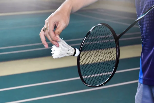 Badminton player is holding white badminton shuttlecock and badminton racket in front of the net before serving it over the net to another side of badminton court. Soft and elective focus.
