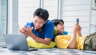 Genç Asyalı yakışıklı oğlanlar yerde uzanıyor, müzik videoları izliyor, cep telefonlarıyla sohbet ediyor ve boş zamanlarını birlikte oturma odasında geçiriyorlar, tüm dünyadaki LGBT aşıkları için konsept..