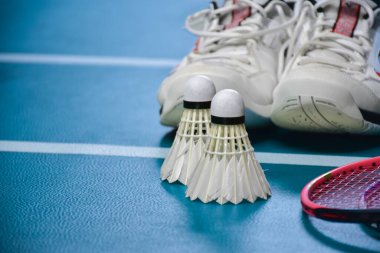 Krem beyazı badminton servis aracı ve kapalı badminton kortunda yeşil zemin üzerinde neon ışıklı raket, bulanık badminton arka plan, kopyalama alanı.