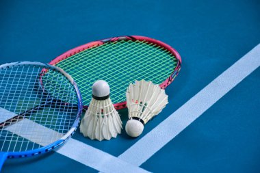 Krem beyazı badminton servis aracı ve kapalı badminton kortunda yeşil zemin üzerinde neon ışıklı raket, bulanık badminton arka plan, kopyalama alanı.