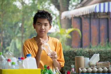 Asyalı genç gönüllü elinde bükülmüş plastik şişelerle çeşitli ayrı garaj kutularının arkasında duruyor, yeni düzenlenmiş, genç çevre hizmetleri ve genç toplum hizmetleri konsepti.