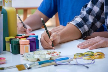 Kadın sanat öğretmeniyle aynı masaya Asyalı çocukların çeşitli resimlerini çizmek için poster rengi kullanmayı öğrenmek, genç ve yetişkin yetiştirmek çocukların okul projelerine yardım etmek..