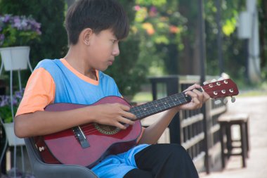 Asyalı tatlı çocuk evinin önünde oturup akustik gitar çalıyor, eğlence amaçlı aktiviteler, serbest zaman aktiviteleri ve dünya çapında erkeklerin hobileri..