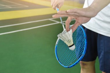 Badminton oyuncusu, raketi ve beyaz kremalı mekikçiyi sahanın diğer tarafına göndermeden önce elinde tutuyor. Tekler konsepte hizmet ediyor..