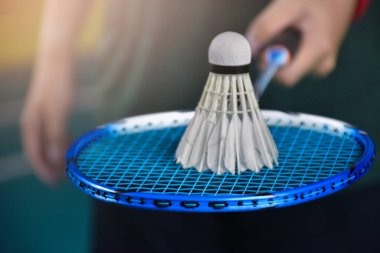 Badminton oyuncusu, raketi sahanın diğer tarafına götürmeden önce, raket ve sicimler üzerine seçici bir şekilde servis hakiminden beyaz kremalı mekik aldı..